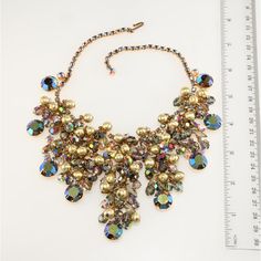 This is part of Chairish’s Costume Jewelry assortment.  Juliana (made by DeLizza & Elster) bib necklace comprised of smoky navette and aurora borealis iridescent rhinestones topped with dangling beads in smoky iridescent and textured gold colors. Setting is gold plated. Unmarked, since only select DeLizza & Elster items were marked with Juliana hang tags. Measures right at 16 inches long; front drop is about 3 inches in the front. Condition is excellent with no missing stones and beautiful gold Iridescent Crystal Necklaces For Party, Elegant Iridescent Necklace For Parties, Elegant Iridescent Crystal Necklaces, Elegant Iridescent Crystal Necklace, Rhinestone Top, Gold Colors, Bib Necklace, Gold Texture, Beaded Dangles