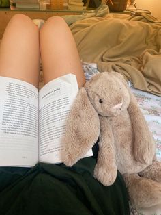 a person laying in bed reading a book with a stuffed animal on their lap next to them