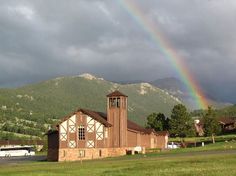 a church with a rainbow in the background and mountains in the foreground on a cloudy day