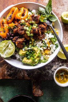 a white bowl filled with rice, black beans and veggies next to lime wedges