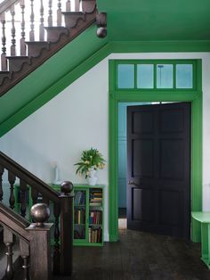 an entryway with green and white walls, black doors and wooden steps leading up to the second floor