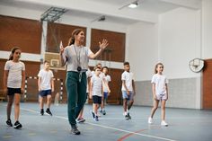 a group of young children playing basketball in a gym with one girl waving to the side