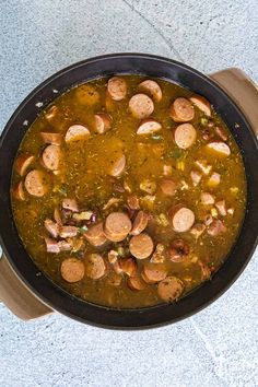 a pan filled with soup and sausages on top of a table next to a cup