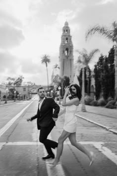 a man and woman are running down the street in front of a building with a clock tower