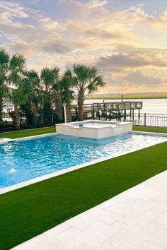 A pool surrounded by artificial turf with a body of water in the background Pools With Artificial Turf, Pool Surrounds, Artificial Turf, Ready For Fall, Green Landscape