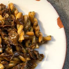 a white plate topped with pasta covered in sauce and mushrooms on top of brown gravy