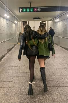 two women walking down a subway platform with their backs to each other, both wearing black boots