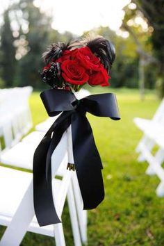 a bouquet of roses tied to the back of a white folding chair with black ribbon