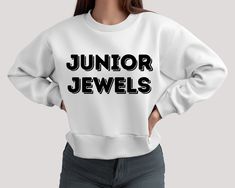 a woman wearing a white sweatshirt with the words junior jewels printed on it in black