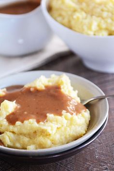 mashed potatoes with gravy in a bowl on a wooden table next to two white bowls