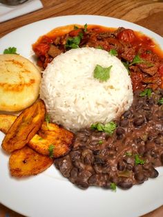 a white plate topped with rice and beans next to potato wedges on top of a wooden table