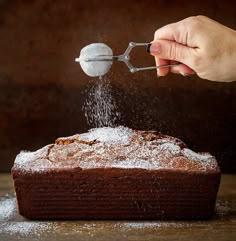 someone sprinkling sugar on top of a chocolate cake with a scoop of icing