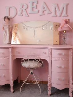 a pink desk with a mirror and doll on it's top, in front of a wall that says dream