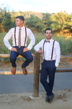 two men wearing ties and suspenders sitting on a fence post