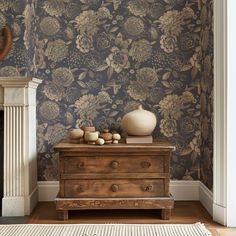 a living room with floral wallpaper and an old dresser in front of the fireplace