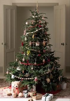 a christmas tree with presents under it and a teddy bear on the floor next to it