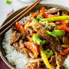 a bowl filled with beef and peppers on top of rice next to chopsticks