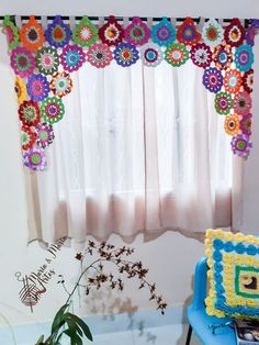 there is a blue chair in front of a window with crocheted flowers on it