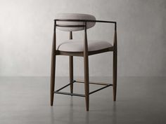 an upholstered bar stool with arms and back rests against a plain wall, in front of a gray background