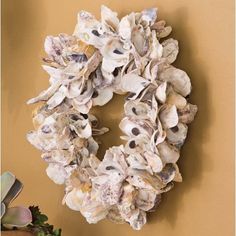 a wreath made out of seashells hangs on the wall next to a potted plant