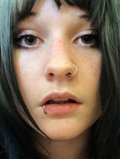 a close up of a person with black hair and piercings on her nose looking at the camera