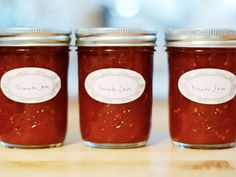 three jars filled with jam sitting on top of a wooden table