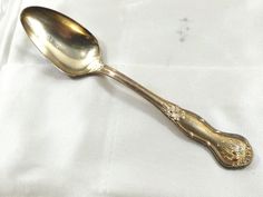 a gold spoon sitting on top of a white cloth covered tablecloth with an ornate design