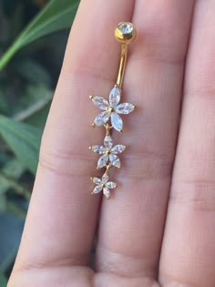 a close up of a person's hand holding a gold nose ring with flowers on it