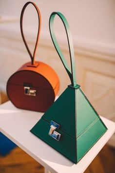 two purses sitting on top of a white table next to each other, one in green and the other in orange