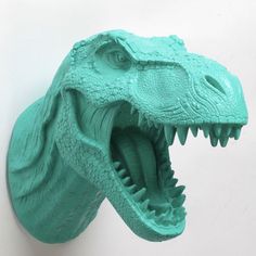 a green plastic dinosaur head on a white wall with it's mouth wide open