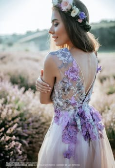 a woman in a dress with flowers on her head standing in a field full of wildflowers