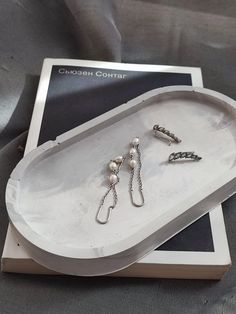 three pairs of earrings sitting on top of a white tray with silver chains and pearls