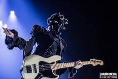 a man in a black outfit holding a white bass guitar and wearing a gas mask