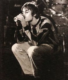 black and white photograph of a man drinking from a cup while sitting on a stool