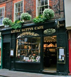 a store front with flowers on the windows and plants growing out of it's roof