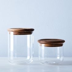 two glass jars with wooden lids on a table