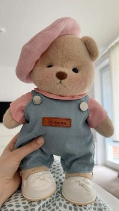 a small teddy bear wearing overalls and a pink hat on top of a bed