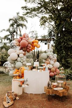 an outdoor dessert table with oranges, white and grey balloons hanging from the ceiling