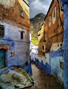 an alley way with blue buildings and mountains in the backgrouds on a cloudy day