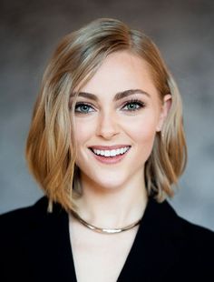 a woman with blonde hair and blue eyes smiles at the camera while wearing a black blazer