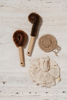 two brushes, a crochet dish cloth and a wooden brush on a white surface