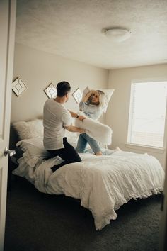 a man and woman sitting on top of a bed in a room with white walls