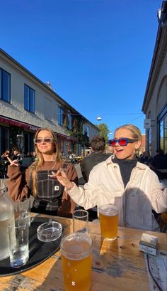 two women sitting at a table with beer in front of them on a sunny day