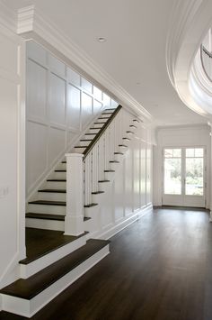 an empty room with wood floors and white railings on the wall, along with stairs leading up to two windows