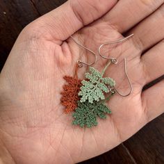 a person's hand is holding three small crocheted leaf earrings in different colors