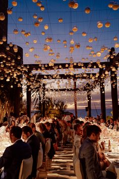 a group of people sitting at tables under lights and lanterns on the ceiling above them