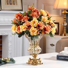 a vase filled with orange and yellow flowers on top of a white table next to a book