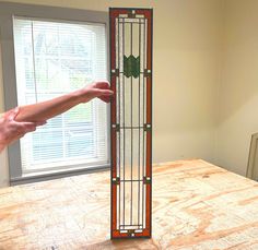 a tall stained glass window sitting on top of a wooden table next to a person's hand