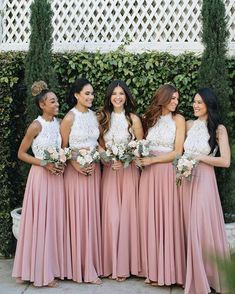 a group of women standing next to each other in front of a wall with greenery