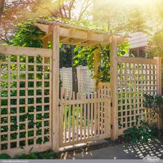 a wooden fence with trelliss in the middle and green plants around it, on a sunny day